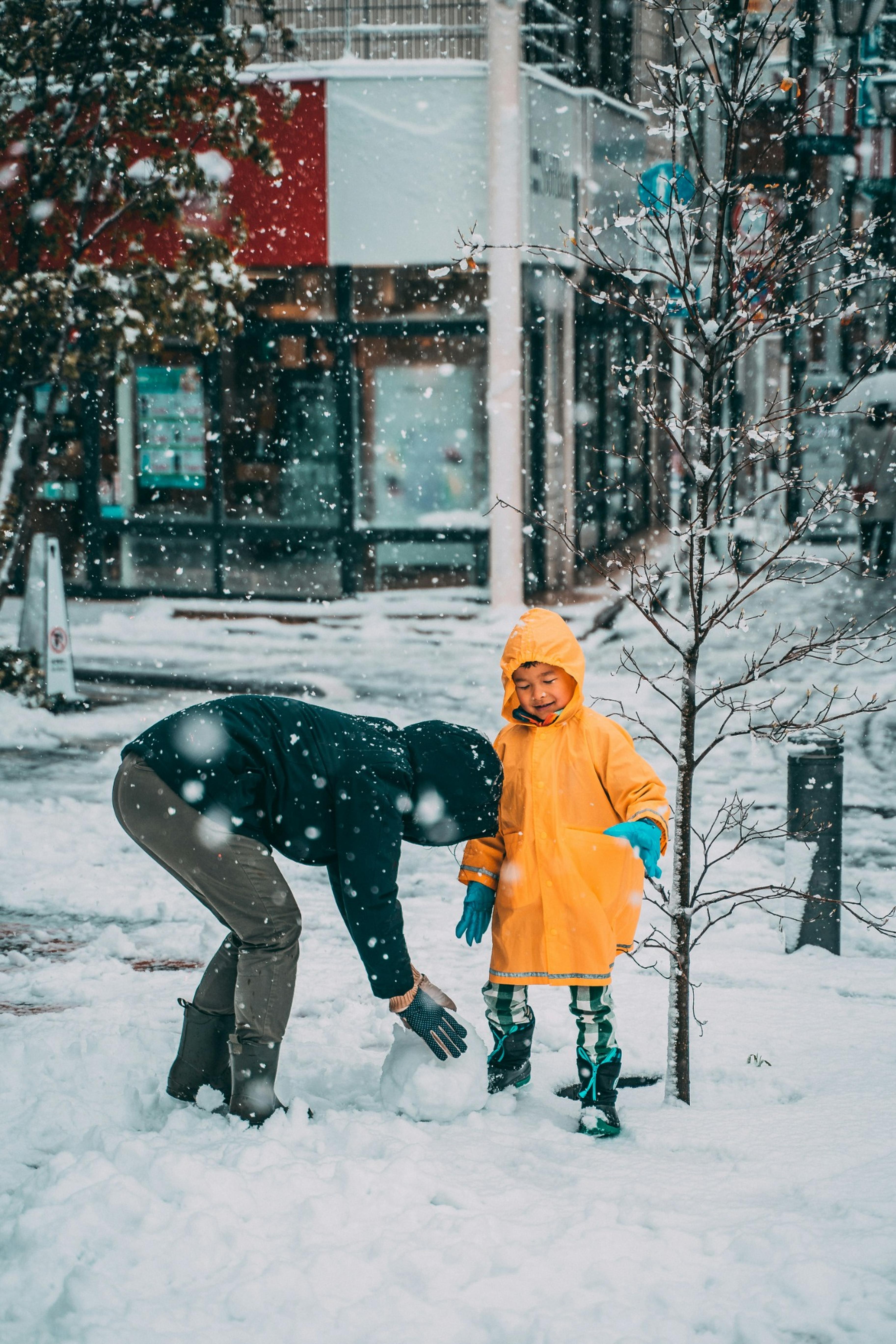 Kind im gelben Regenmantel und blauen Handschuhen beim Schneebauen – Kinder Winterschuhe: Perfekt für die kalte Jahreszeit + Last-Minute-Sale! ❄️👢