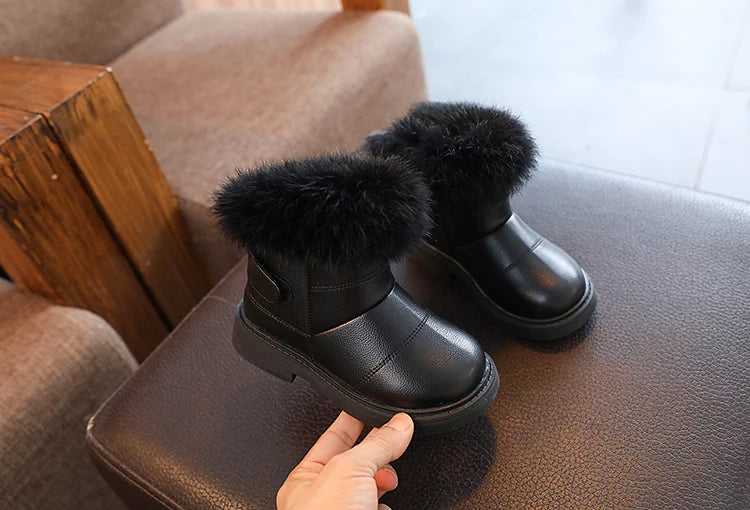 Zwei Paar schwarze Kinder Winterstiefel auf dunkler Oberfläche.
